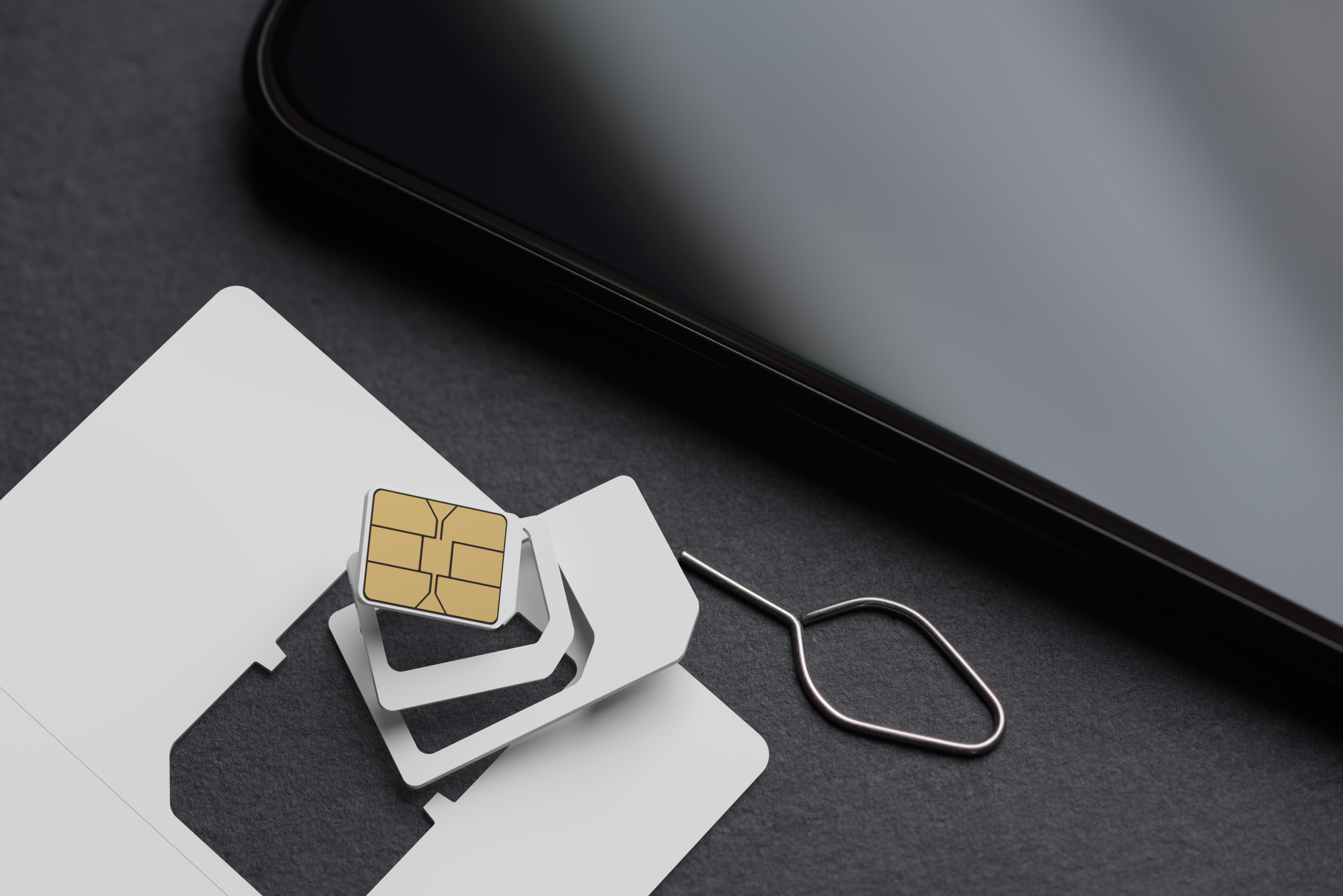 Blank white SIM card with different precut sizes and smartphone on black slate. 3D rendering and photo
